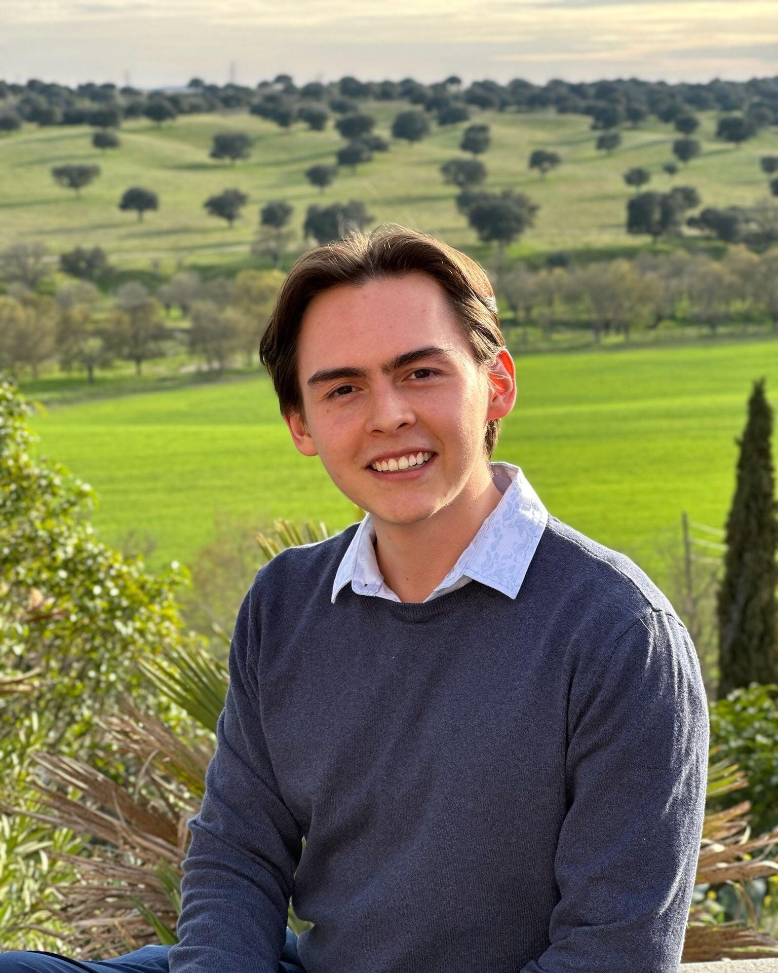 Juan Felipe smiling, with green fields and holm oaks behind him.